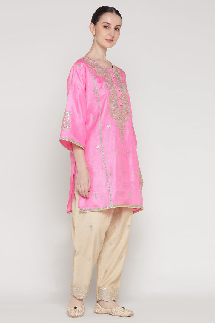 Woman wearing a pink kurta with gold embroidery on a white background