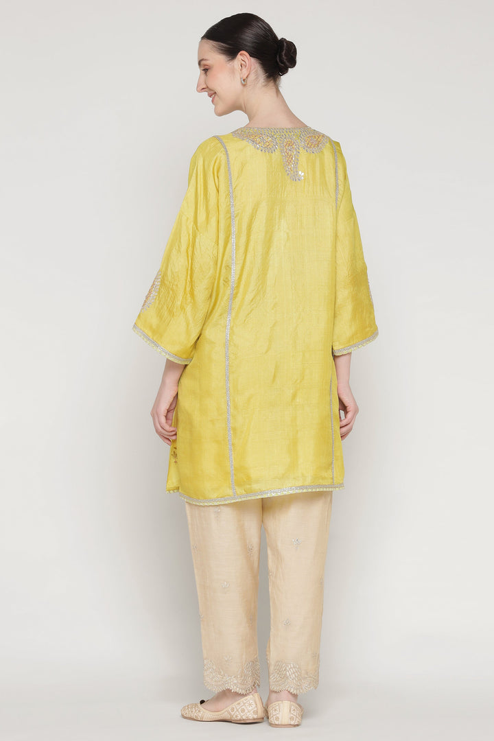 Woman wearing a yellow kurta with beige pants on a white background