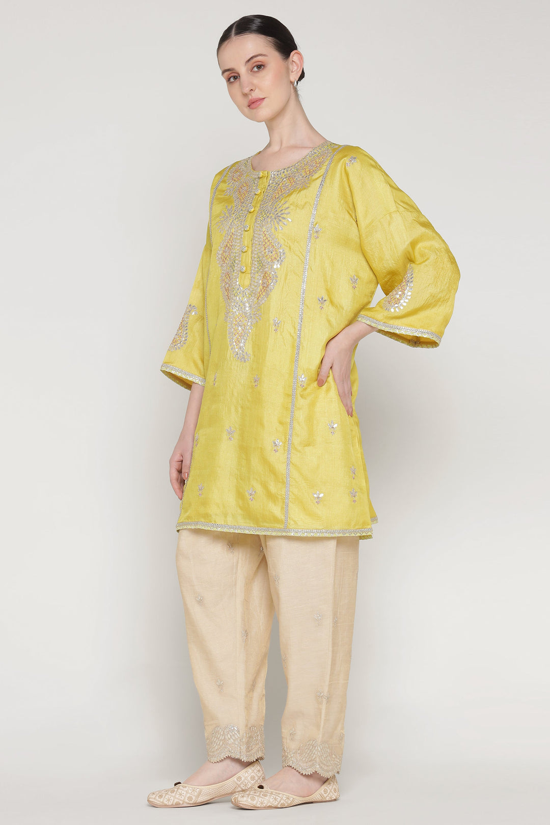 Woman wearing a yellow embroidered top and beige pants on a white background