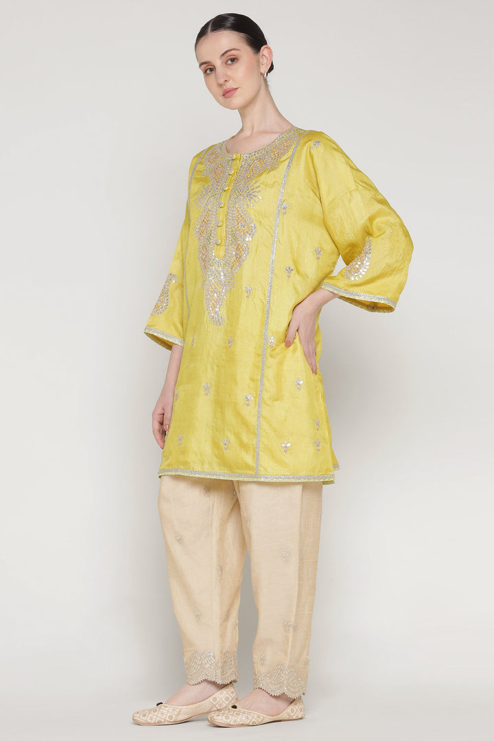 Woman wearing a yellow embroidered top and beige pants on a white background