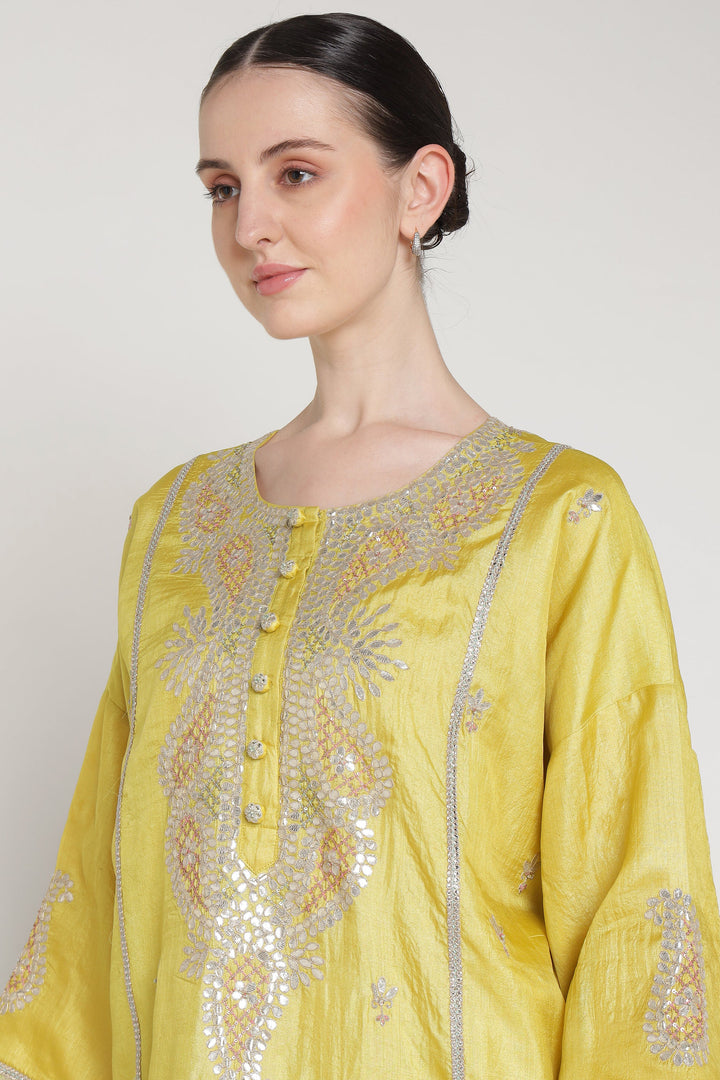 Woman wearing a yellow embroidered traditional outfit against a plain background