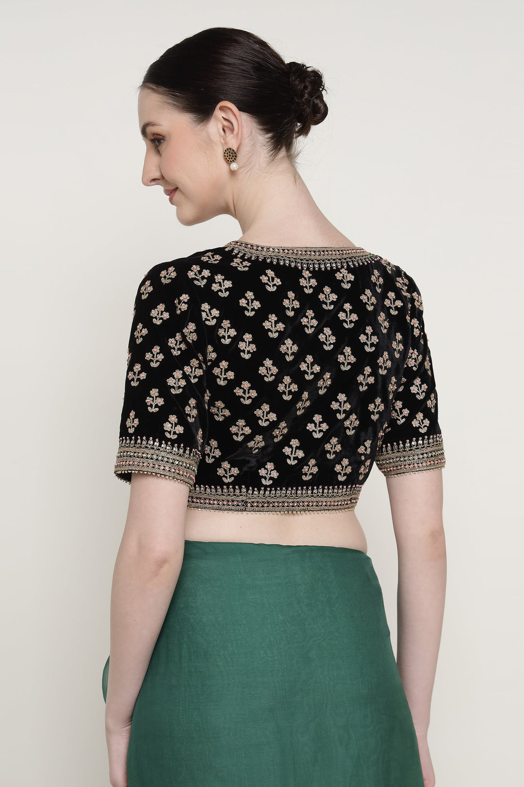 Woman wearing a black embroidered blouse with gold details on a plain background