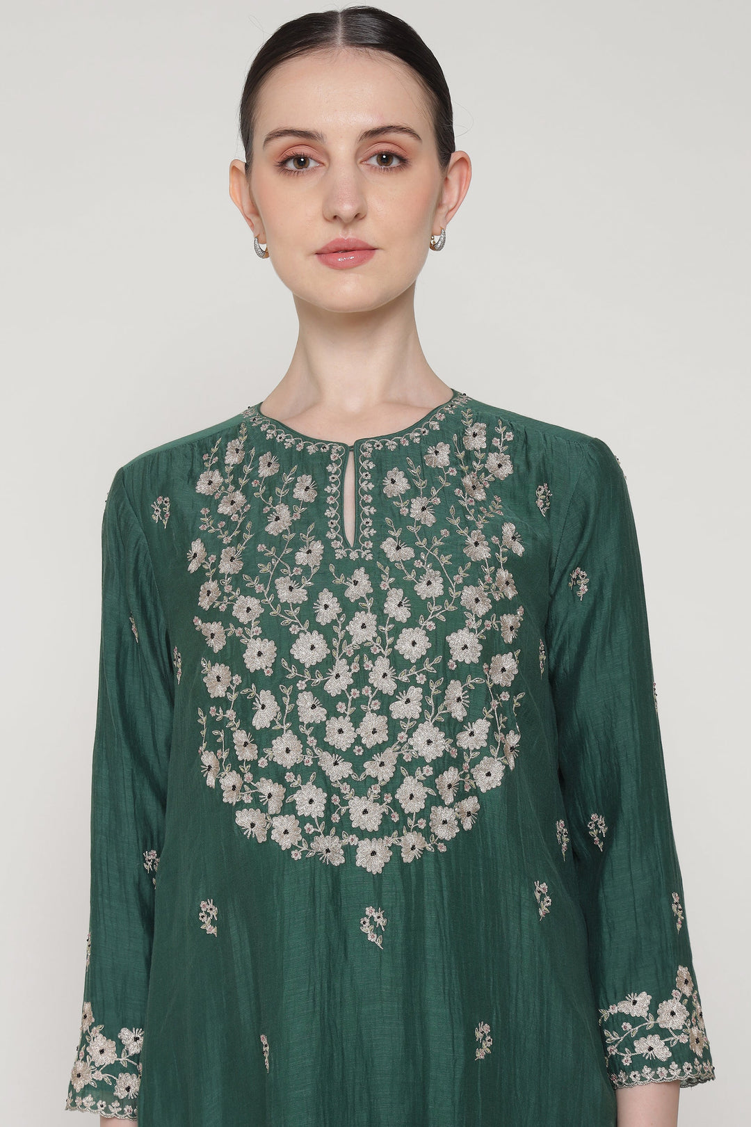 Woman wearing a green floral embroidered dress against a white background