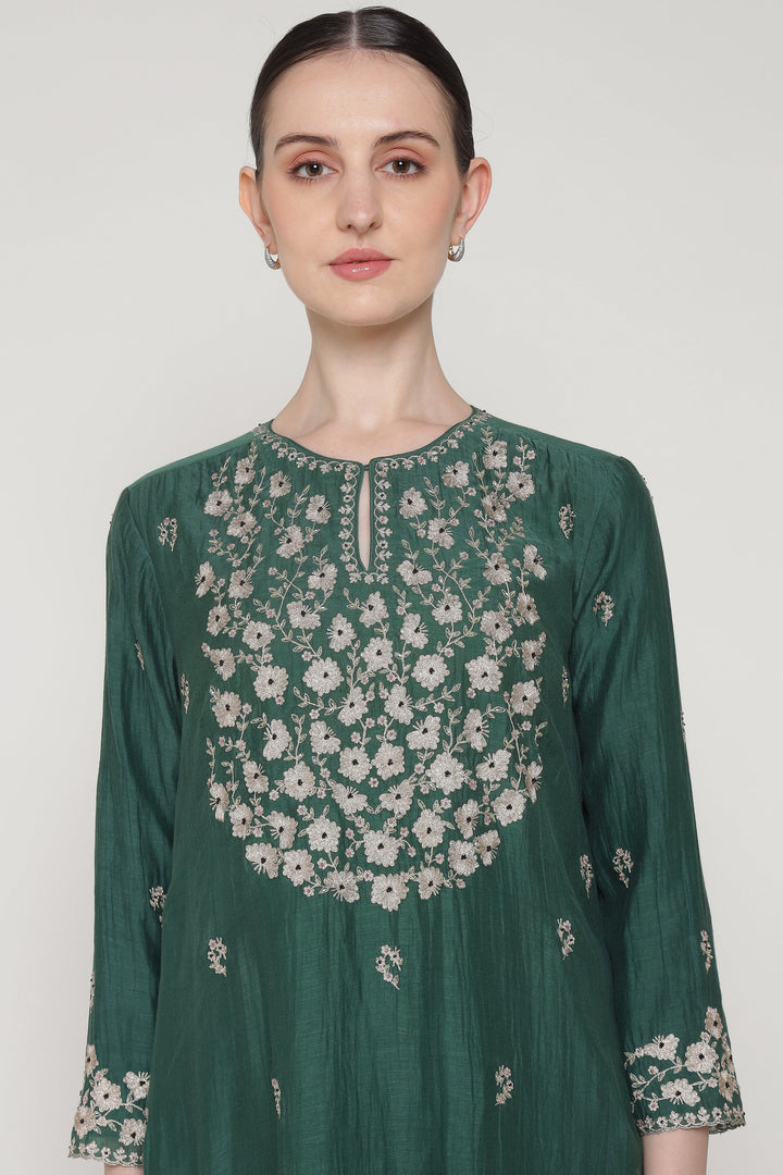 Woman wearing a green floral embroidered dress against a white background