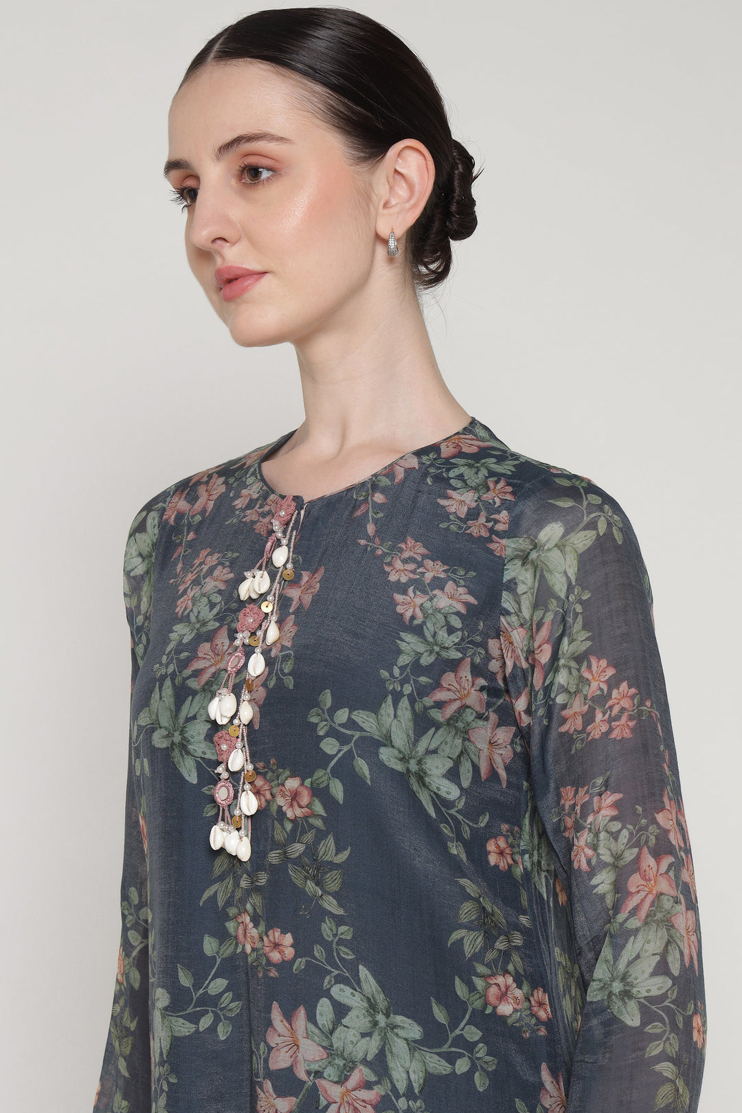 Woman wearing a dark floral blouse with buttons on a plain background