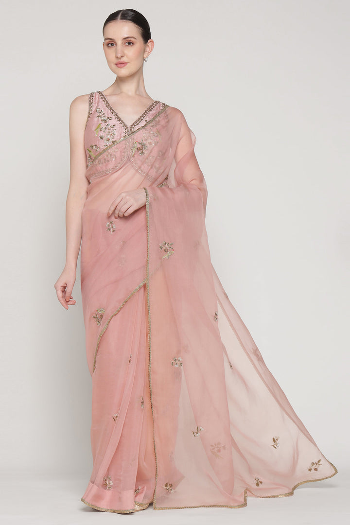 Woman wearing a pink saree with intricate designs on a white background