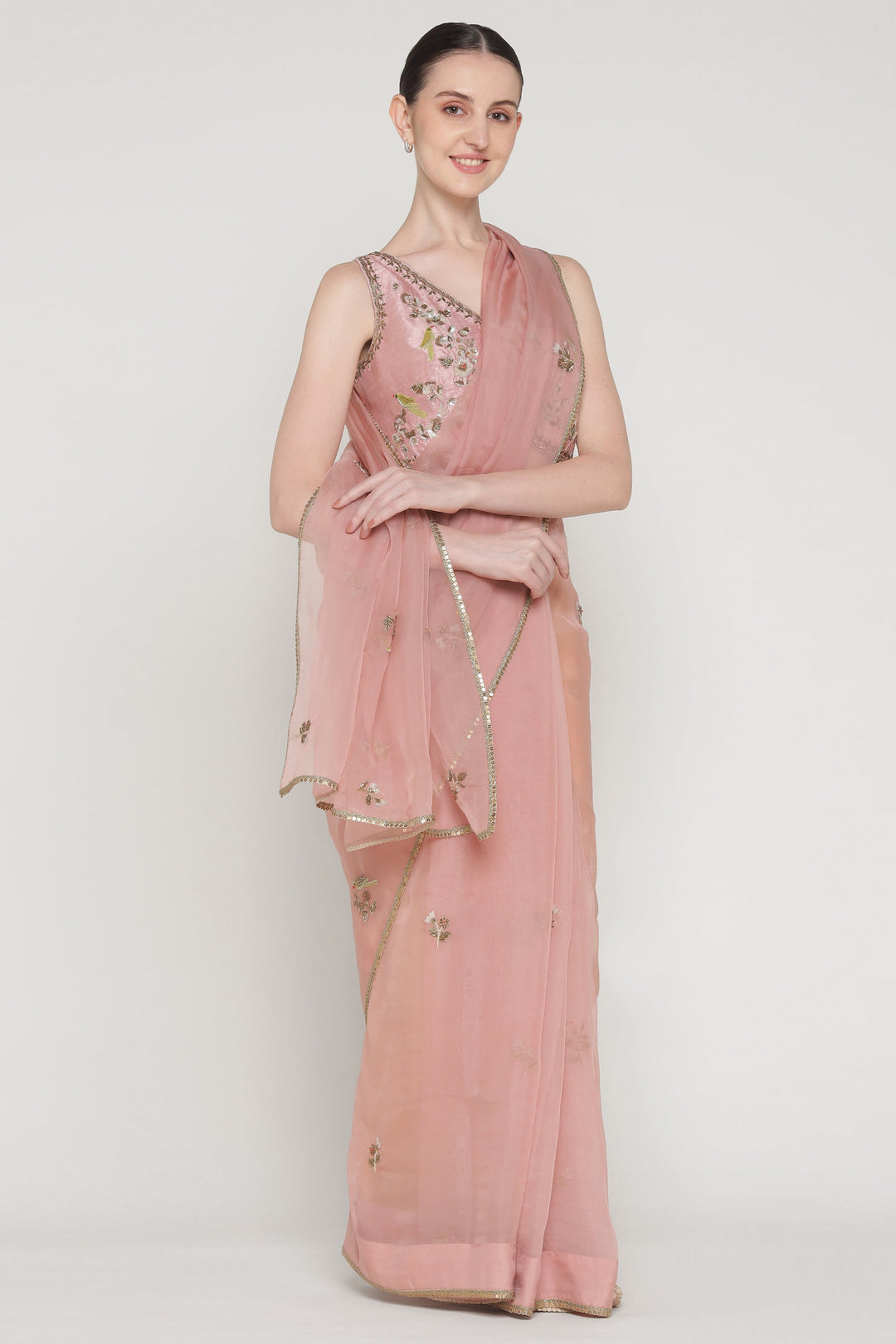 Woman wearing a pink saree with floral embellishments on a white background