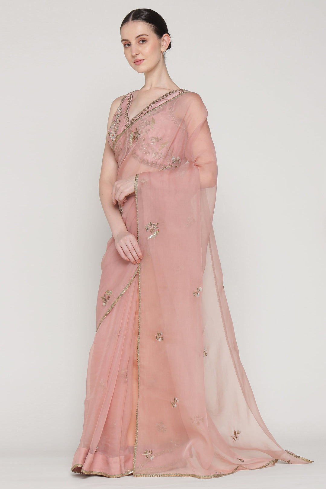 Woman wearing a pink saree with intricate designs on a white background