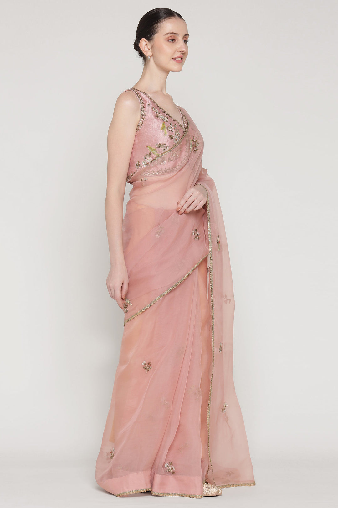 Woman wearing a pink saree with intricate designs on a white background