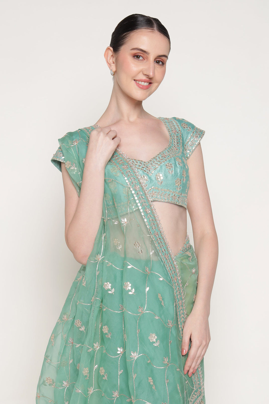 Woman wearing a light green saree with a matching blouse on a white background