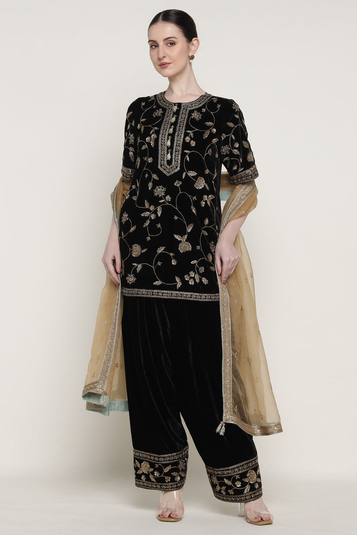 Woman wearing a black embroidered outfit with beige dupatta on a white background