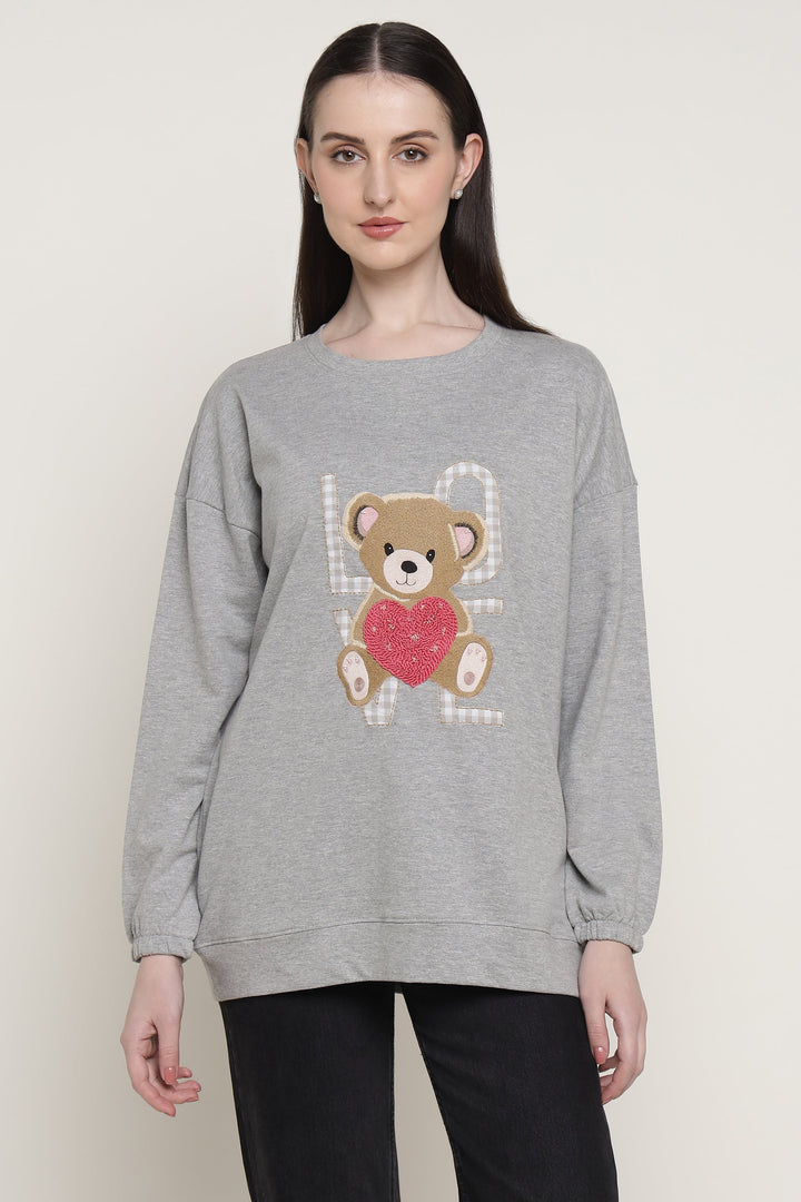 Woman wearing a gray sweatshirt with a teddy bear design on a plain background