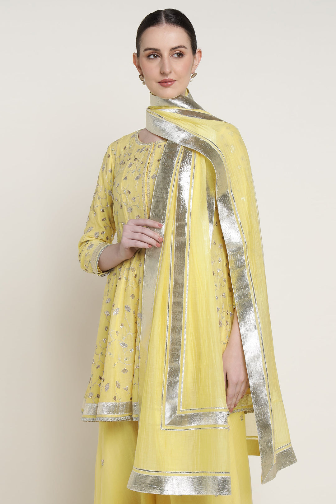 Woman wearing a yellow traditional outfit with a silver border on a plain background