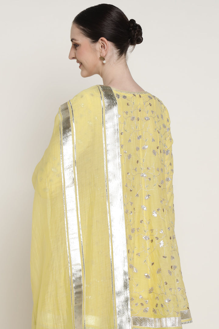 Woman wearing a yellow saree with silver details on a plain background