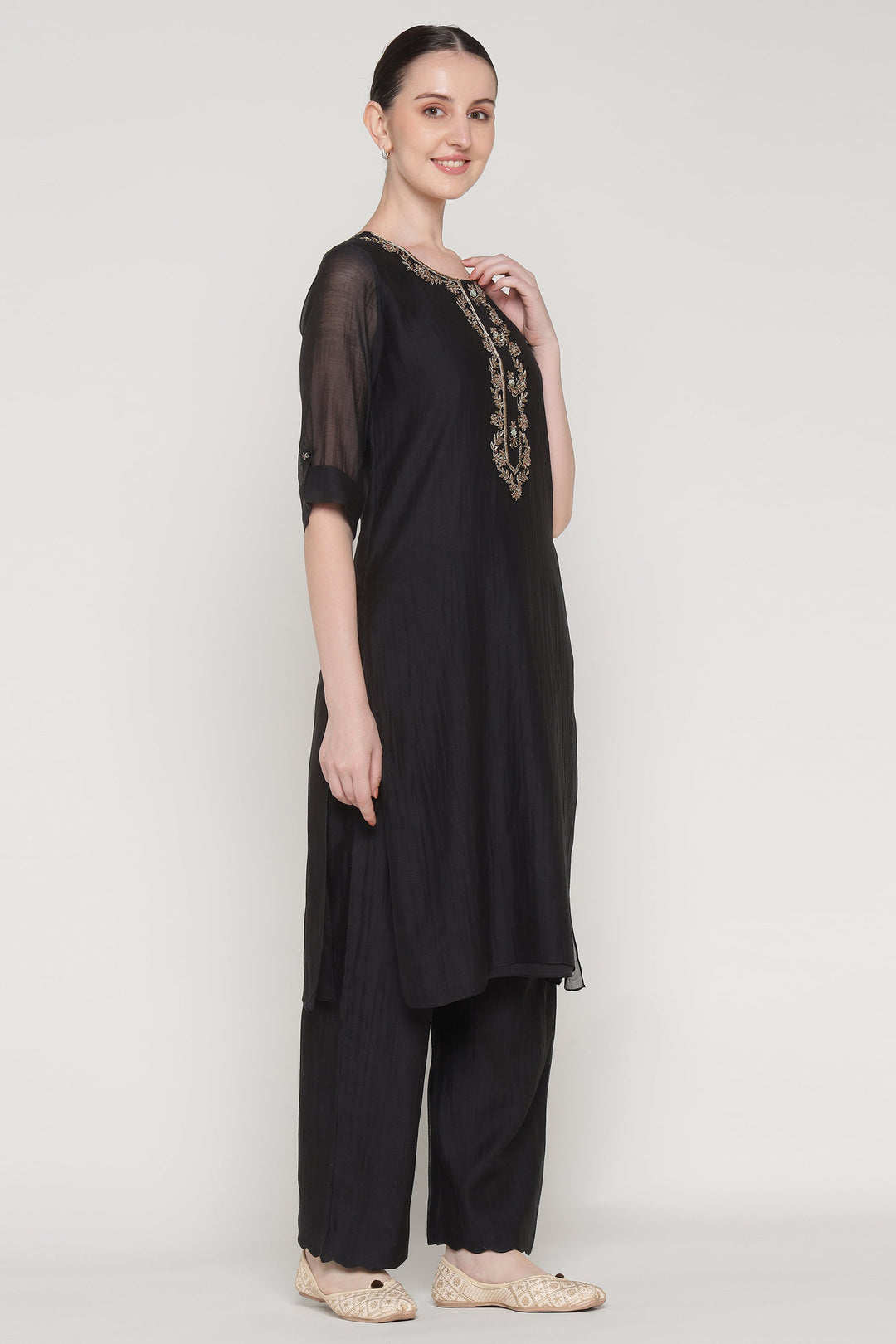 Woman wearing a black outfit with a sheer top and embroidered details on a white background