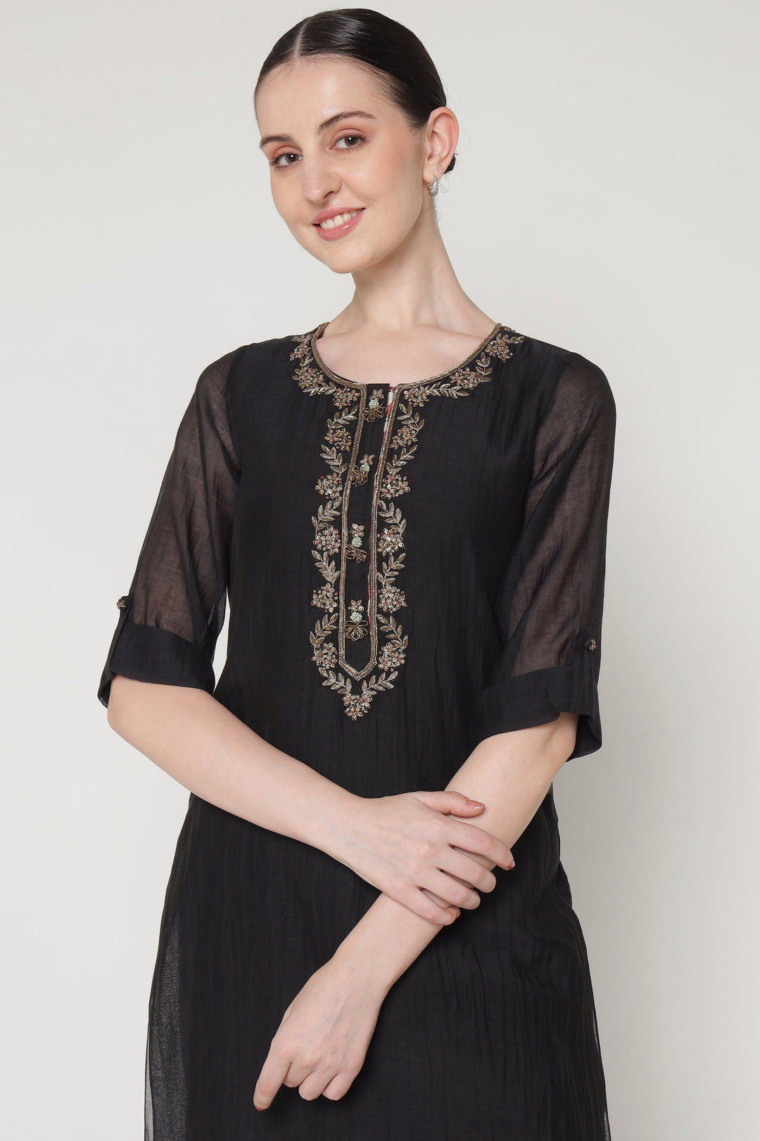 Woman wearing a black dress with gold embroidery on a white background