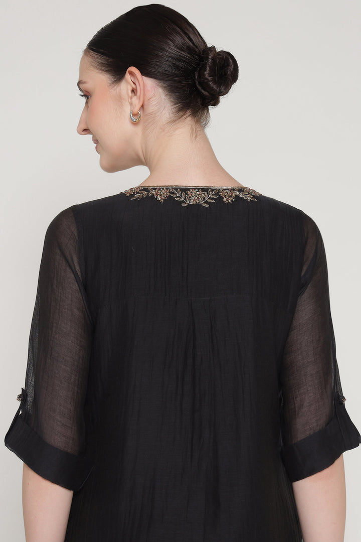 Black sheer top with embroidered neckline worn by a model on a plain background