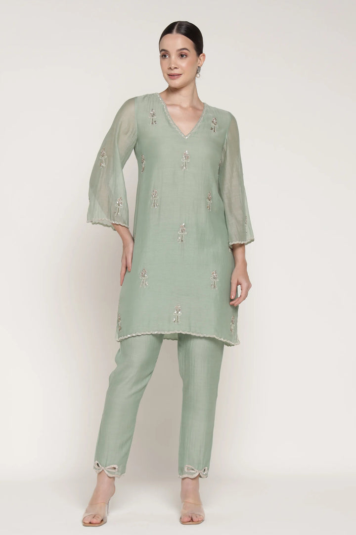 Woman wearing a light green traditional outfit with a plain background