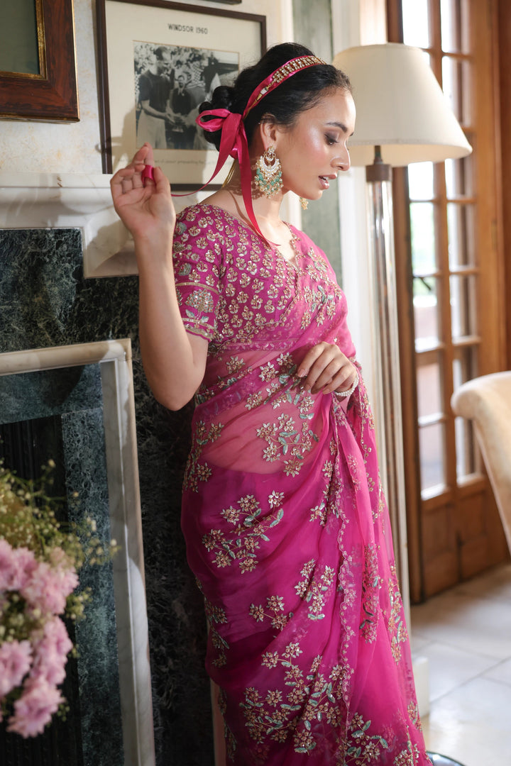 Woman in a pink saree standing in a room with decor elements.