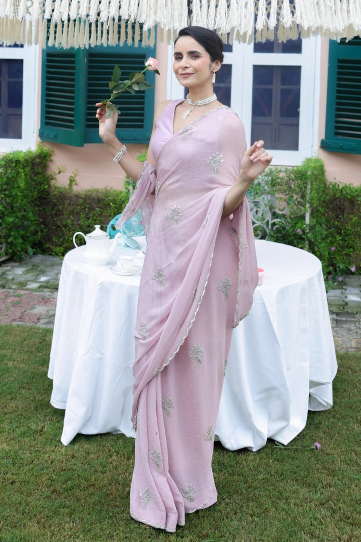 Woman in a pink saree holding an ornate white parasol outdoors.