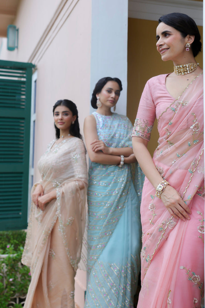 Three women in traditional sarees standing outdoors near a building.