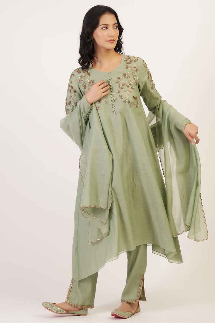 Woman wearing a light green traditional outfit with floral embroidery on a white background