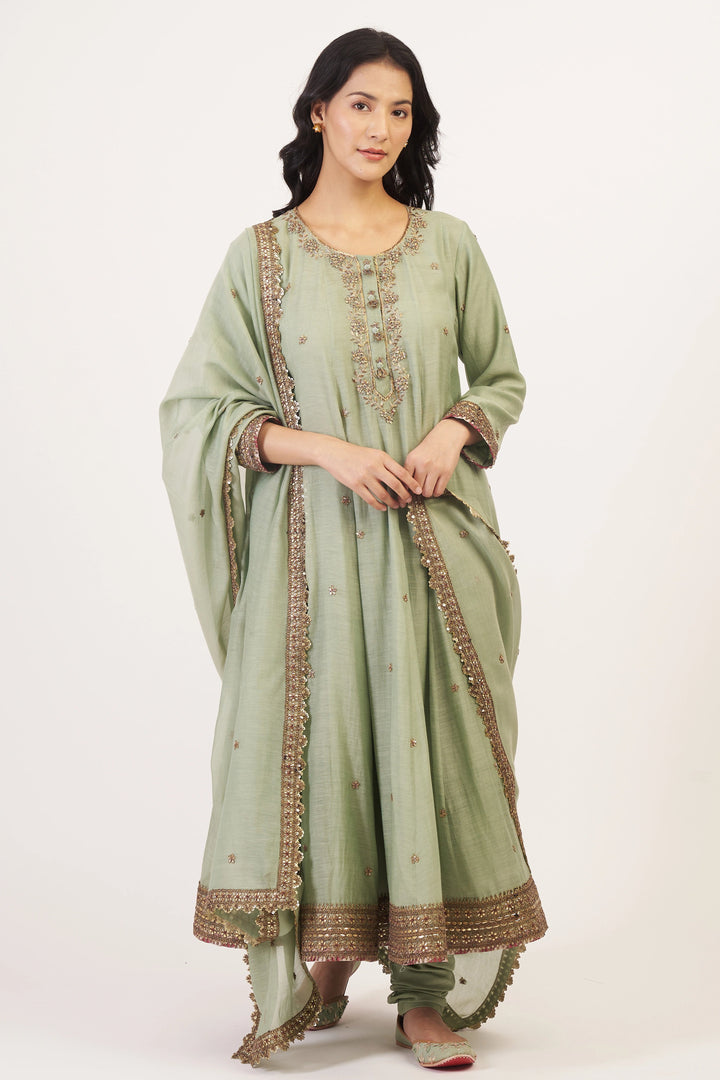 Woman wearing a light green traditional outfit with embroidery on a white background