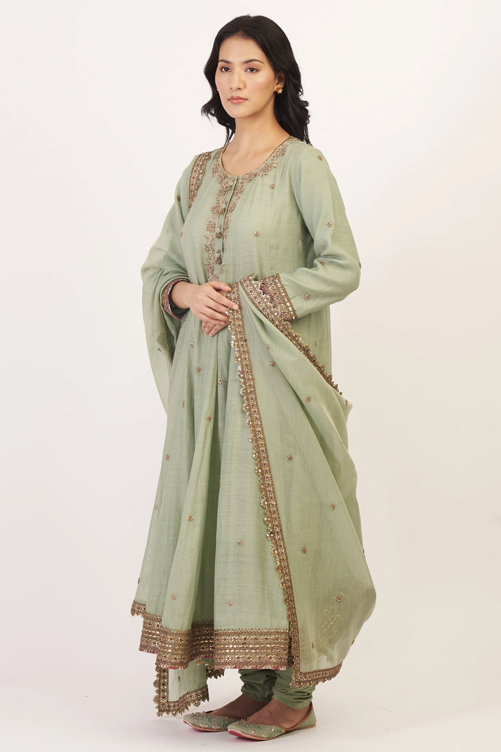Woman wearing a light green traditional outfit with intricate patterns on a white background