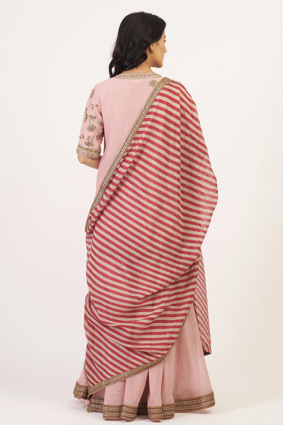 Woman wearing a pink and red striped saree with a plain background
