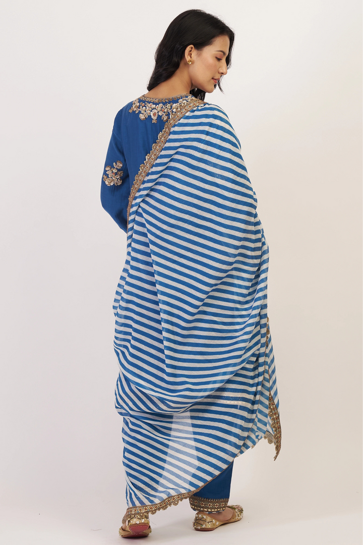 Woman wearing a blue and white striped saree with gold embroidery on a white background
