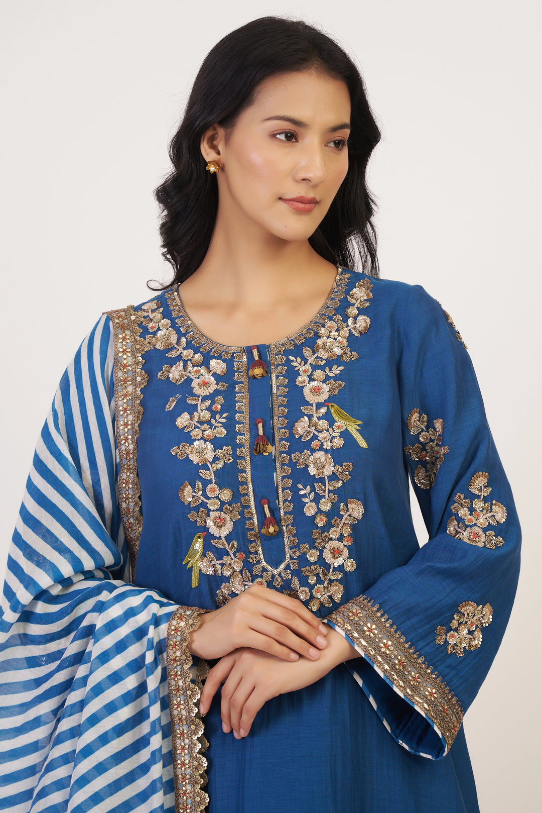 Woman wearing a blue embroidered traditional outfit with a white background