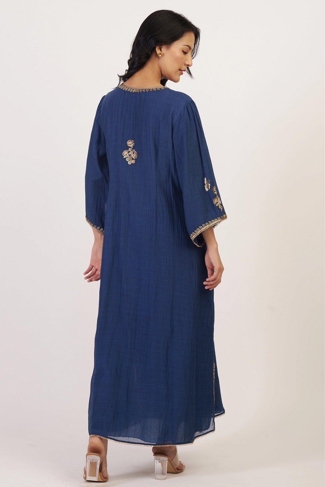 Woman wearing a blue dress with gold embroidery on a white background