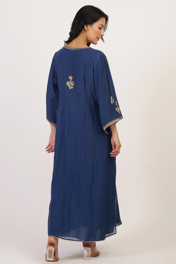 Woman wearing a blue dress with gold embroidery on a white background