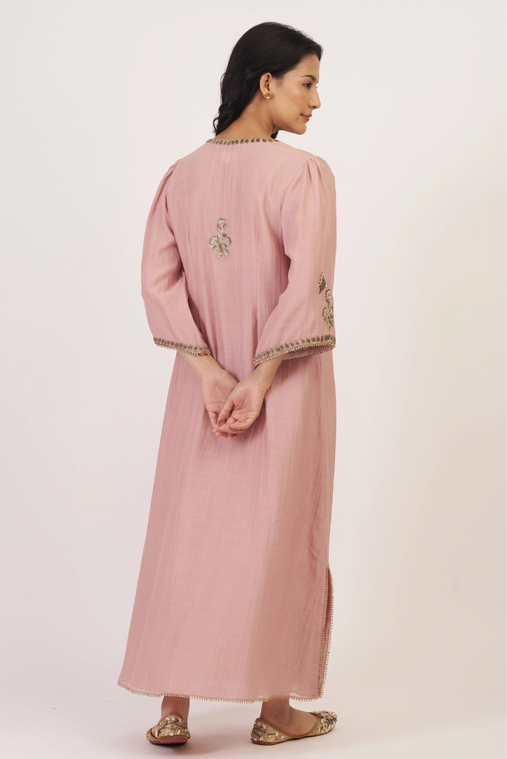 Woman wearing a pink dress with intricate designs on a white background