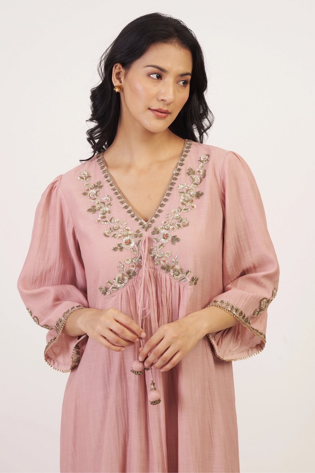 Woman wearing a pink dress with floral embroidery on a white background