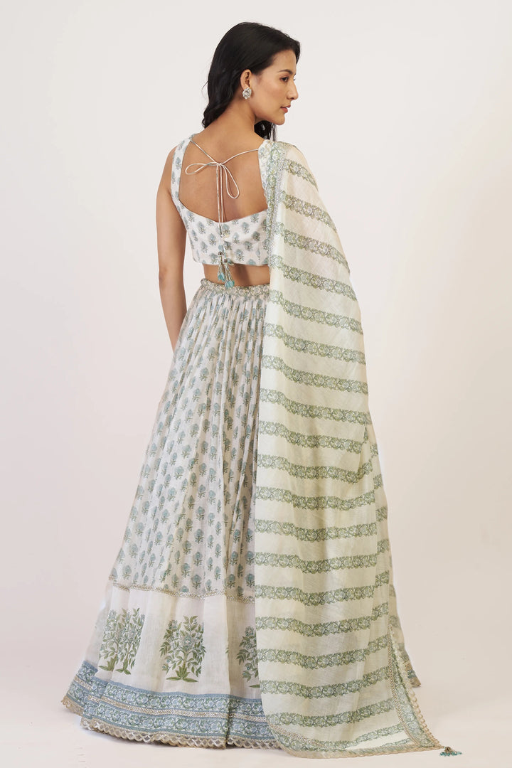 Woman wearing a traditional outfit with a white and green patterned dupatta on a plain background