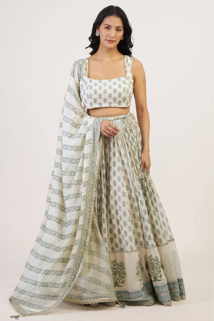 Woman wearing a traditional outfit with a white and green patterned saree on a plain background