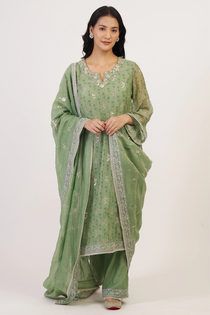 Woman wearing a green traditional outfit with intricate patterns on a white background