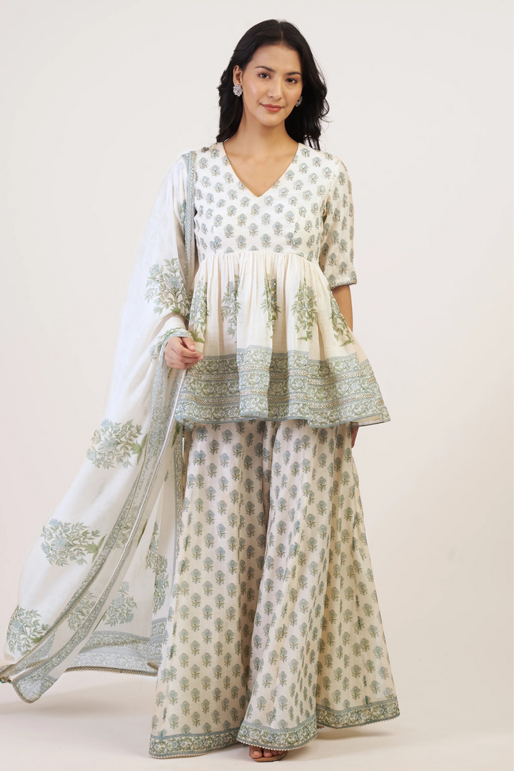 Woman wearing a traditional outfit with a white and green pattern on a plain background