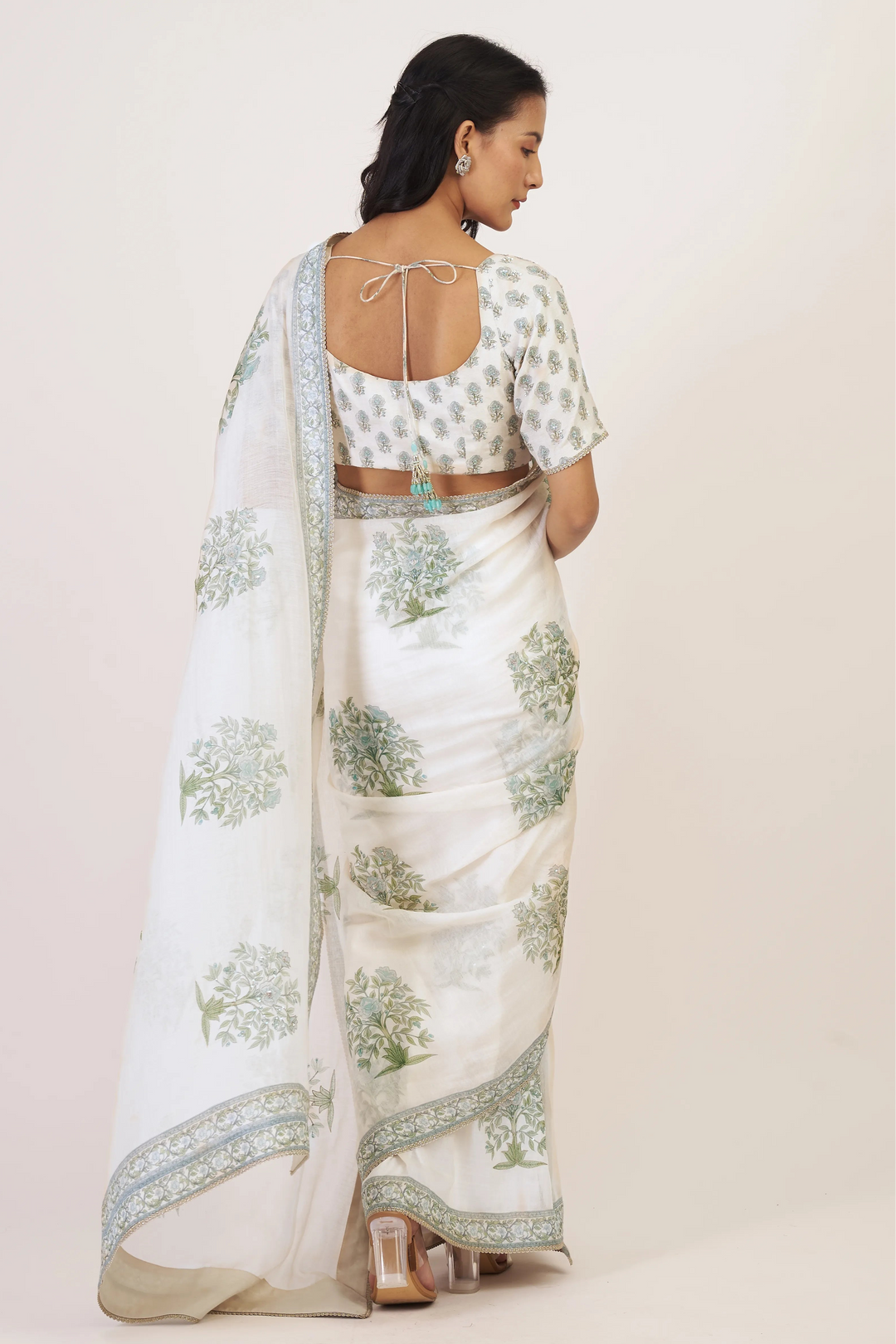 Woman wearing a white saree with green floral patterns on a plain background