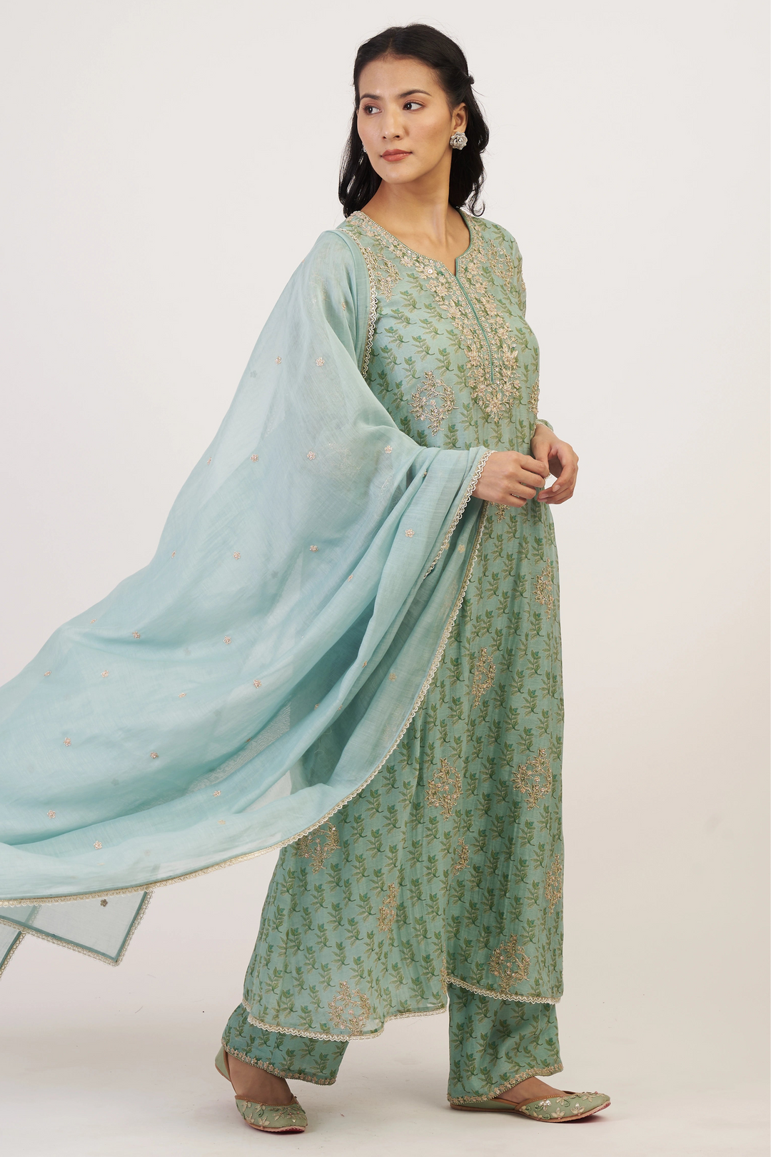Woman wearing a green traditional outfit with a light blue dupatta on a white background