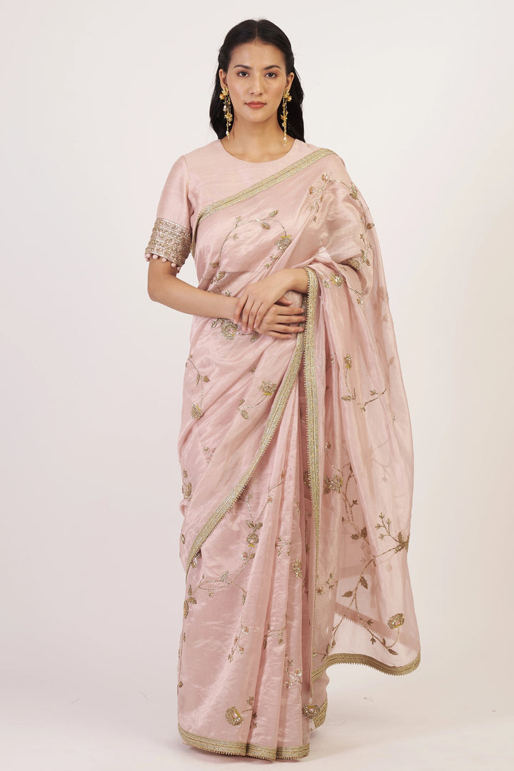 Woman wearing a light pink saree with gold accents on a white background