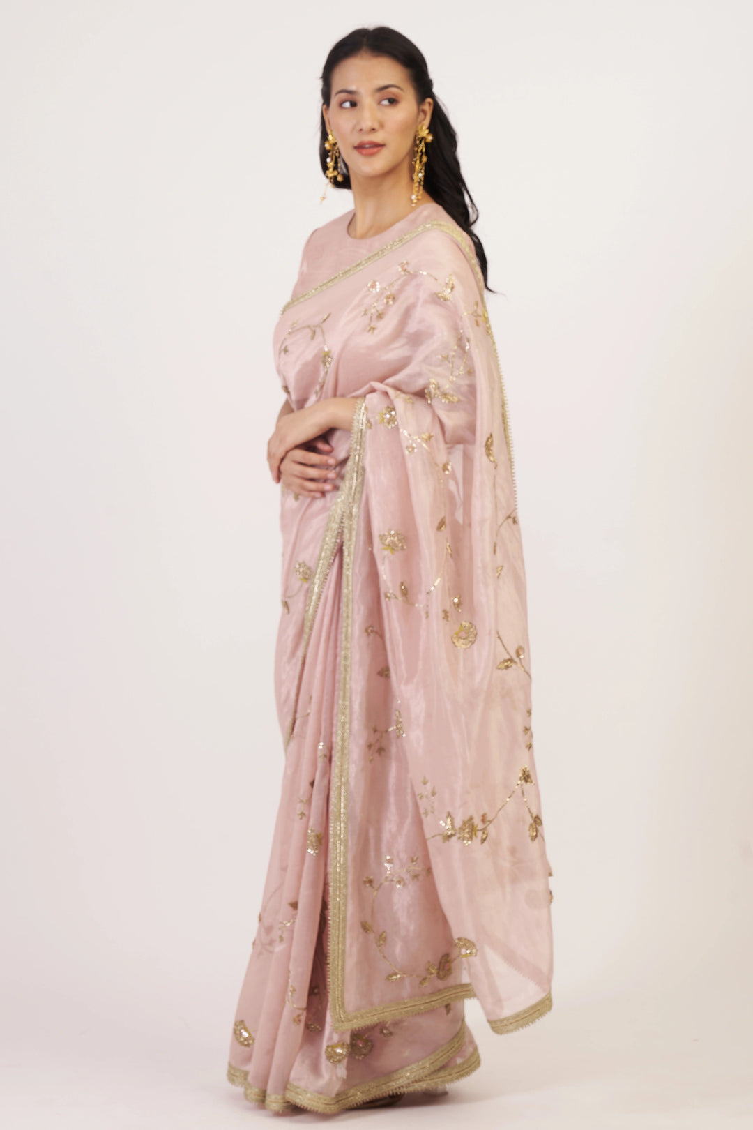 Woman wearing a light pink saree with gold embroidery on a white background