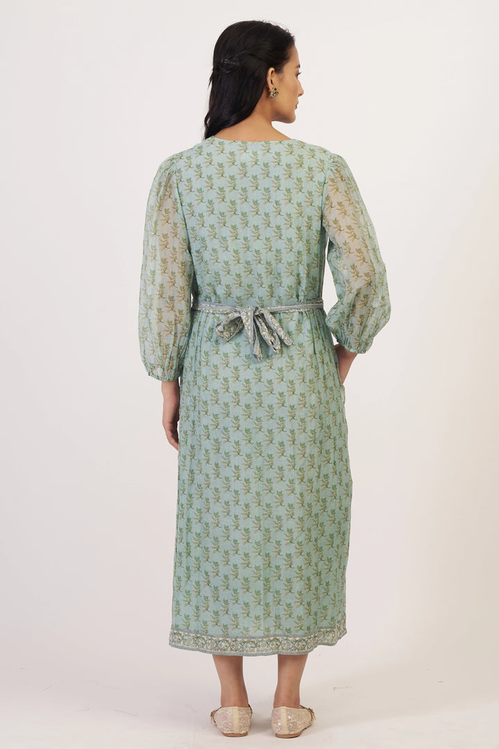 Woman wearing a green patterned dress with sheer sleeves on a white background