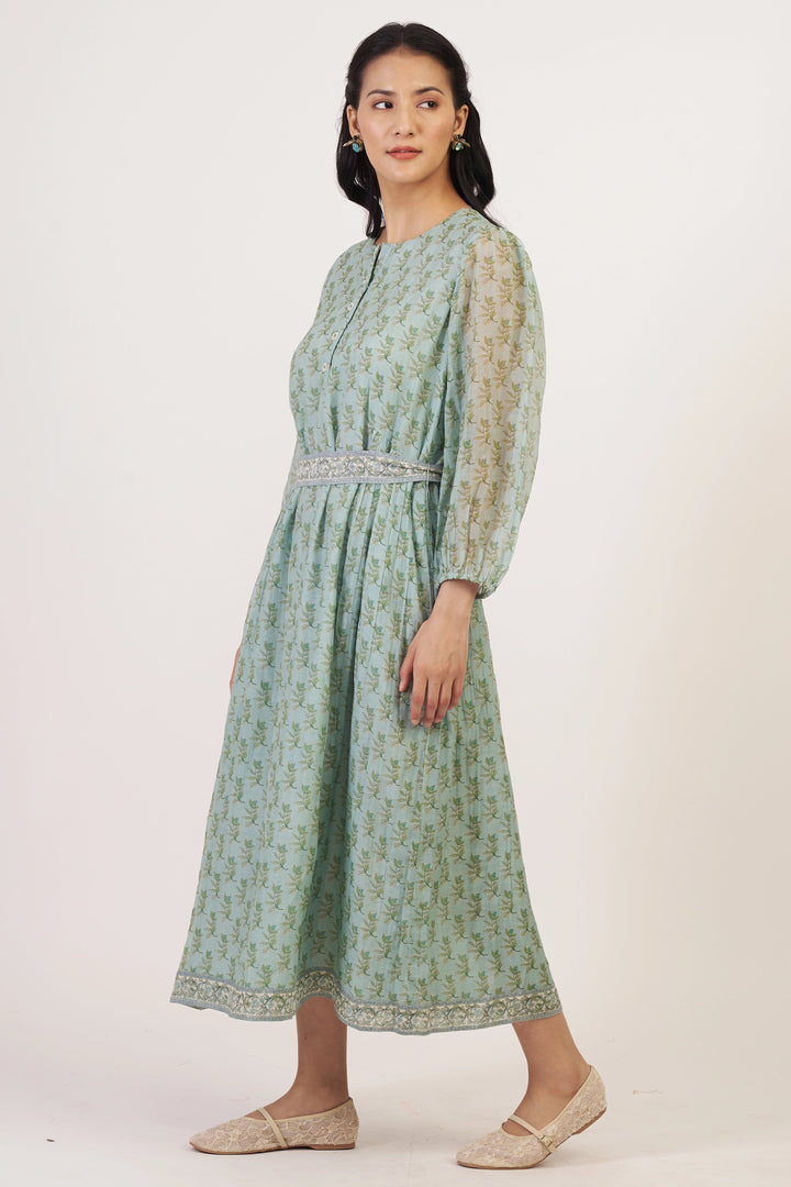 Woman wearing a green patterned dress with sheer sleeves on a white background
