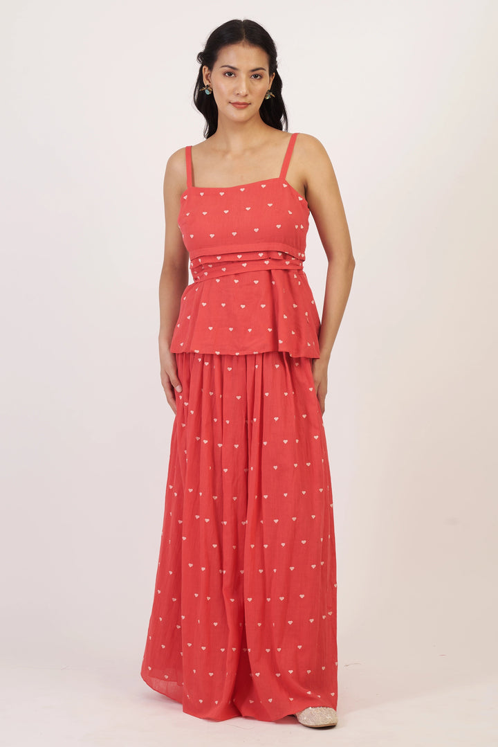 Woman wearing a coral dress with white patterns on a light pink background