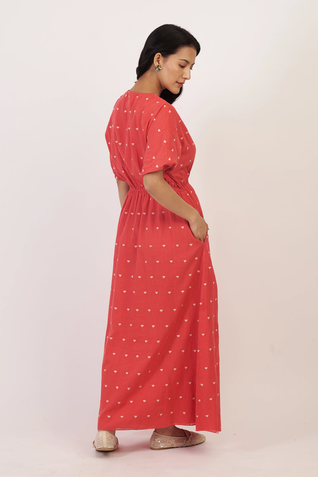 Woman wearing a red dress with white patterns on a light pink background