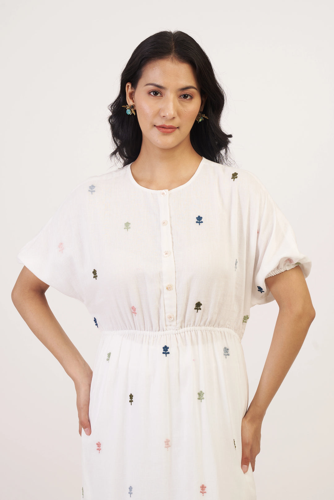 Woman wearing a white dress with small colorful floral patterns on a plain background