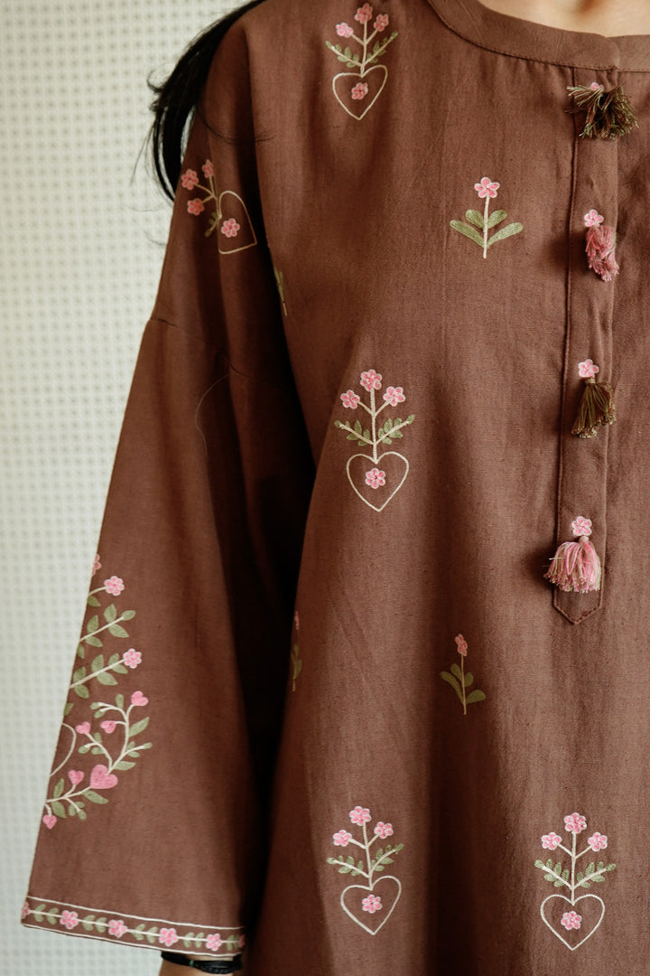 Brown dress with floral embroidery on a textured wall background